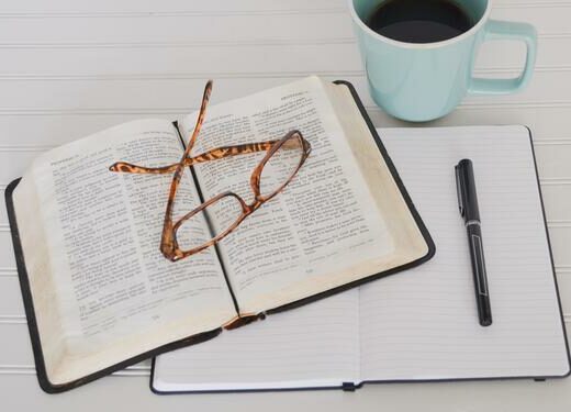 Notebook, book, and glasses on a table next to a cup of coffee