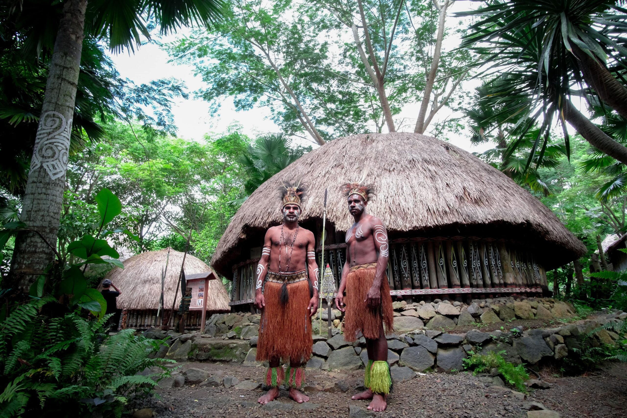Indigenous males standing in the jungle in front of a hut